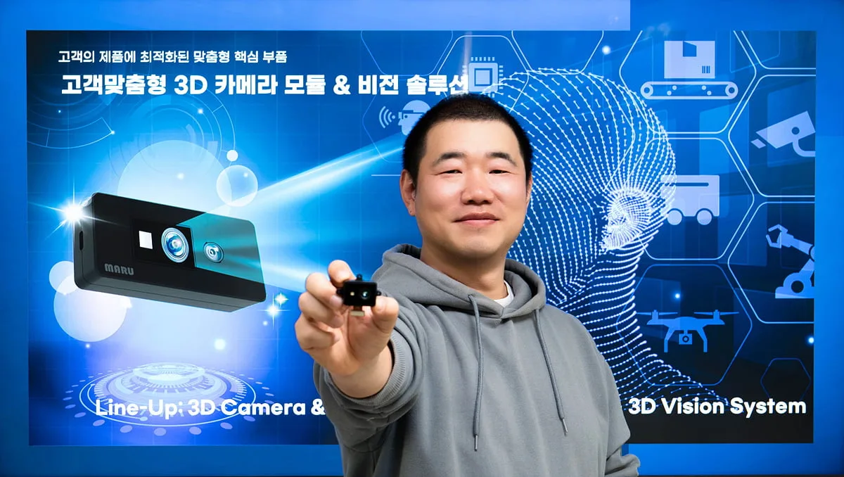 CEO Kim Dae-hee holding a small camera module toward the camera in front of a MARU product graphic